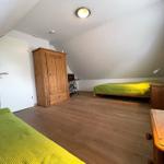 Schlafzimmer mit grünem Bett, Holzmöbeln und Holzboden unter schrägem Dach