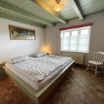 Schlafzimmer mit Bett, Stuhl und Fenster. Holzdecke und Parkettboden.