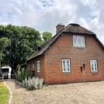 Rotes Backsteingebäude mit Strohdach und weißen Fenstern. Gartenweg und Badehaus im Hintergrund.