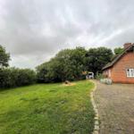 Roter Backsteinbau mit strohgedecktem Dach, umgeben von Grünfläche und Bäumen.