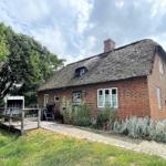 Rotes Backsteingebäude mit Strohdach, Terrasse und Garten. 