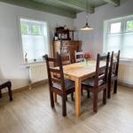 Esszimmer mit Holztisch, Stühlen und Fenstern. Holzfußboden und Deckenbalken.