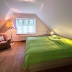 Schlafzimmer mit Bett, Sessel und Fenster mit Blick nach draußen.