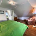 Schlafzimmer mit grünem Bett, Sessel und Stehlampe unter schrägen Dachschrägen.