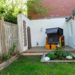 Hinterhof mit Garten, Holzgeländer, Sitzgelegenheit und Blumenbeete.