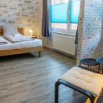 Schlafzimmer mit Doppelbett, Holzboden und Fenstern mit Jalousien.