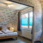 Schlafzimmer mit Doppelbett, Fenstern mit blauen Jalousien und weiß verputzten Ziegelwänden.