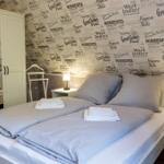 Schlafzimmer mit Doppelbett, zwei Nachttischen und Wandtapete mit Reisestichworten.