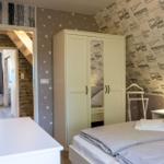 Schlafzimmer mit Doppelbett, Kleiderschrank und Wand mit Reiseaufdrucken.