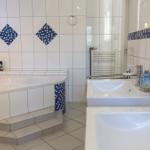 Badezimmer mit Badewanne, zwei Waschbecken und blauen Mosaikfliesen an den Wänden.