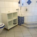 Badezimmer mit Badewanne, Toilette und Regal. Blaue Mosaikfliesen an der Wand.