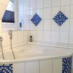 Bad mit Whirlpool, blauen Mosaikfliesen und Fenster mit Jalousie.