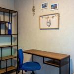 Arbeitszimmer mit Schreibtisch, blauer Stuhl und Regal an der Wand.