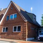 Rotes Backsteingebäude mit Dach und Fenstern, daneben Parkplatz mit Schildern und Auto.