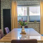 Esszimmer mit Holztisch, Stühlen und Fenster mit Vorhängen.