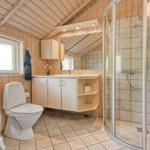Badezimmer mit Dusche, Waschbecken und Toilette. Holzwände und Fliesenboden.