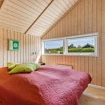 Schlafzimmer mit Holzwand, Bett mit rotem Decken und grünen Kissen, Fenster mit Blick auf Außenbereich.