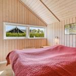 Schlafzimmer mit Holzwand und Dachfenster. Bett mit roter Bettdecke. Wandbild und Nachttische.