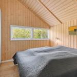 Schlafzimmer mit Holzwand, Doppelbett und Fenster mit Blick auf Bäume.
