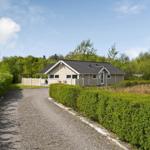Ein Haus mit grauem Dach und Holzfassade steht hinter einem Kiesweg und grünen Hecken.