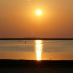 Sonnenuntergang über ruhigem Wasser mit Silhouette einer Person auf Stand-Up-Paddle.