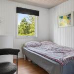 Schlafzimmer mit Bett, Fenster und Stuhl. Wand mit Bild und Pflanze.