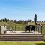 Terrasse mit Liegestuhl, Tisch und Stühlen. Blick auf grüne Landschaft und Himmel.