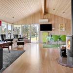 Wohn- und Essbereich mit Kamin, Holzdecke und großem Fensterblick auf Garten.