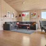 Wohnzimmer mit Holzwand, grauem Sofa, Sessel und großem Fenster.