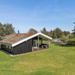 Haus mit Grasdach, Terrasse und Garten. Umgeben von Bäumen und Grasflächen.