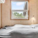 Ein Schlafzimmer mit Holzwänden, einem Fenster und einem Bett mit grauer Bettwäsche.