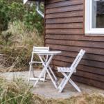 Weiße Tisch- und Stühle auf Terrasse neben Holzhaus mit Fenster