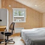 Schlafzimmer mit Bett, Schreibtisch und Fenster. Holzwände und -decke.