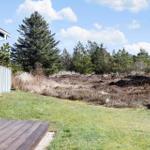 Haus mit Holzterrasse, Grasfläche und Wald im Hintergrund.