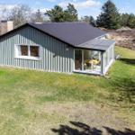 Ein graues Haus mit Glasveranda und Garten. Im Inneren ist ein Tisch mit gelben Stühlen zu sehen.