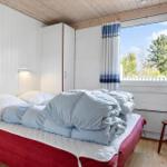 Schlafzimmer mit Bett, Kleiderschrank und Fenster mit Blick auf Bäume.