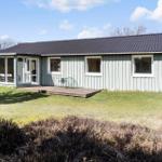 Ein Haus mit Holzfassade, Terrasse und Glasfront. Grünfläche und Sträucher im Vordergrund.