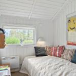Schlafzimmer mit weißem Holzpaneelen, Fenster und Bett mit Kissen.
