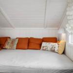 Ein Sofa mit orangefarbenen Kissen und gemusterten Kissen in einem Raum mit weißem Holzverkleidung.