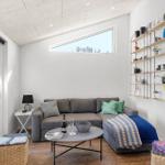Wohnzimmer mit Sofa, Couchtisch und Wandregal. Fenster und Tür führen nach draußen.