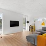 Wohnzimmer mit grauem Sofa, gelber Stehlampe und Fernseher an der Wand.