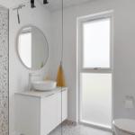 Badezimmer mit Dusche, Waschbecken und Toilette. Terrazzo-Wand und Fenster.