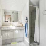Badezimmer mit Dusche, Waschbecken und Spiegel. Weiße Holzwände und Fliesen.