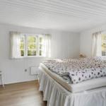 Schlafzimmer mit Bett, Fenstern und Stuhl. Weiße Wände und Holzboden.