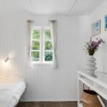 Ein Zimmer mit weißem Holzverkleidung, Fenster, Bett und Vase mit Blumen.