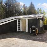 Ein kleines Haus mit offener Tür, Grill und Terrasse im Wald.