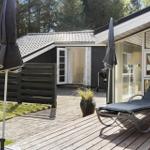 Terrasse mit Liegestuhl und geschlossenen Sonnenschirmen neben einem Haus mit Glasfront.