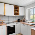 Küche mit weißen Schränken, Holzoberflächen und Fensterblick auf Grün.