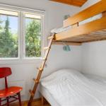 Ein Schlafzimmer mit Doppelstockbett, roter Stuhl und Fensterblick auf Bäume.