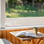 Ein Tisch mit Buch und Tasse vor einem Fenster mit Blick auf den Garten.